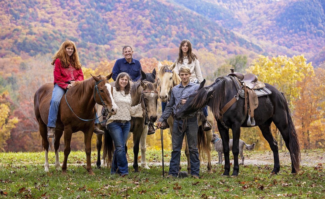 The Thompson family with their horses and dogs in front of fall mountains