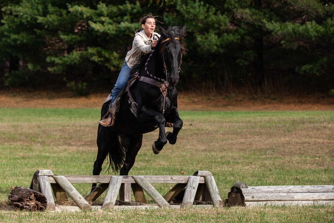 Rider taking a black horse over a cross-country log jump