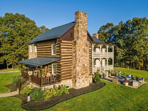The historic log main house at Harborwood Farm with a stone chimney and wraparound porches